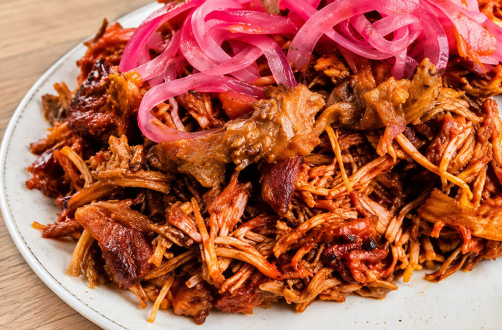 Cochinita pibil de cerdo desmechado con cebolla encurtida.